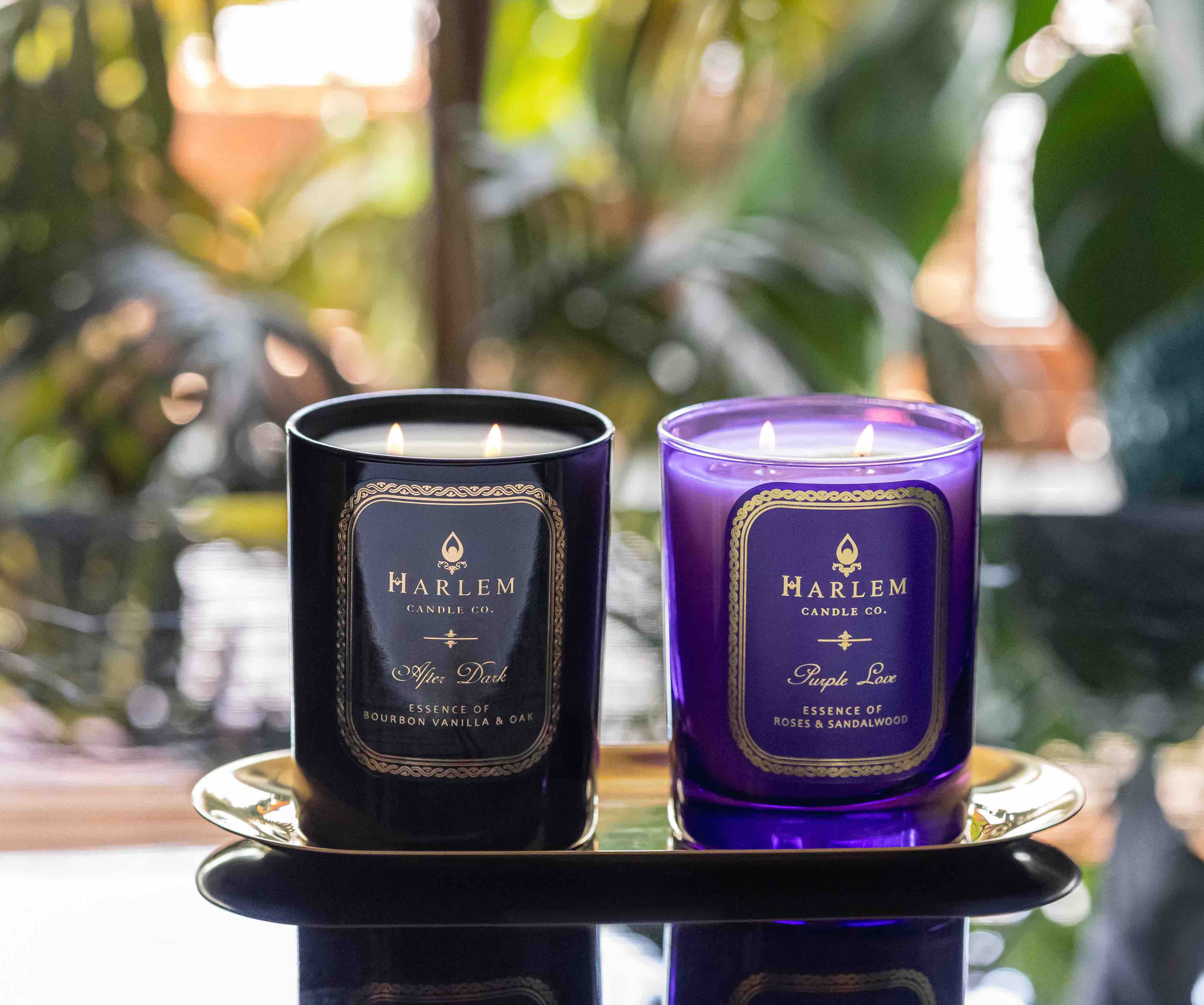 This is an image of our Purple Love and After Dark candles pictured on a table with plants behind.