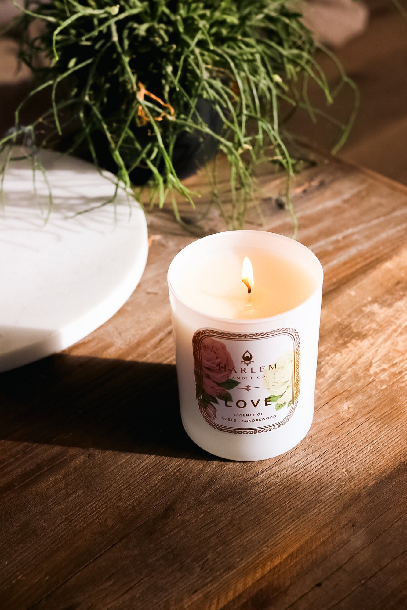 This is an image of the "Love" Luxury Candle on a wooden table with greenery in the background.