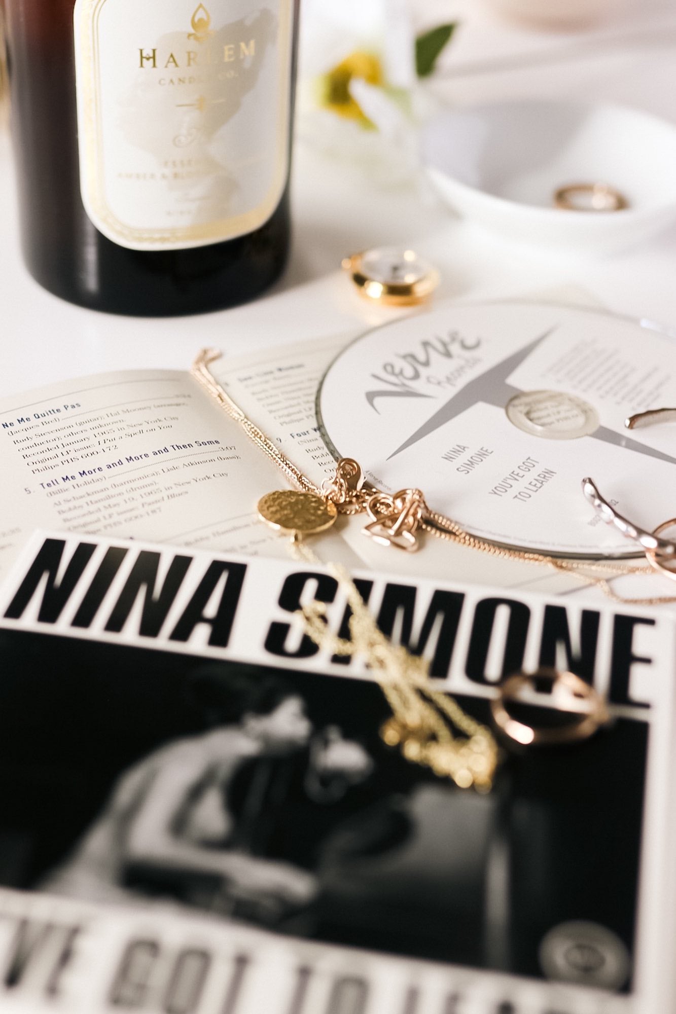 This is a lifestyle image of the Nina candle picture next to a Nina Simone, CD and some jewelry. The candle is illuminated with a CD  and album cover in the image