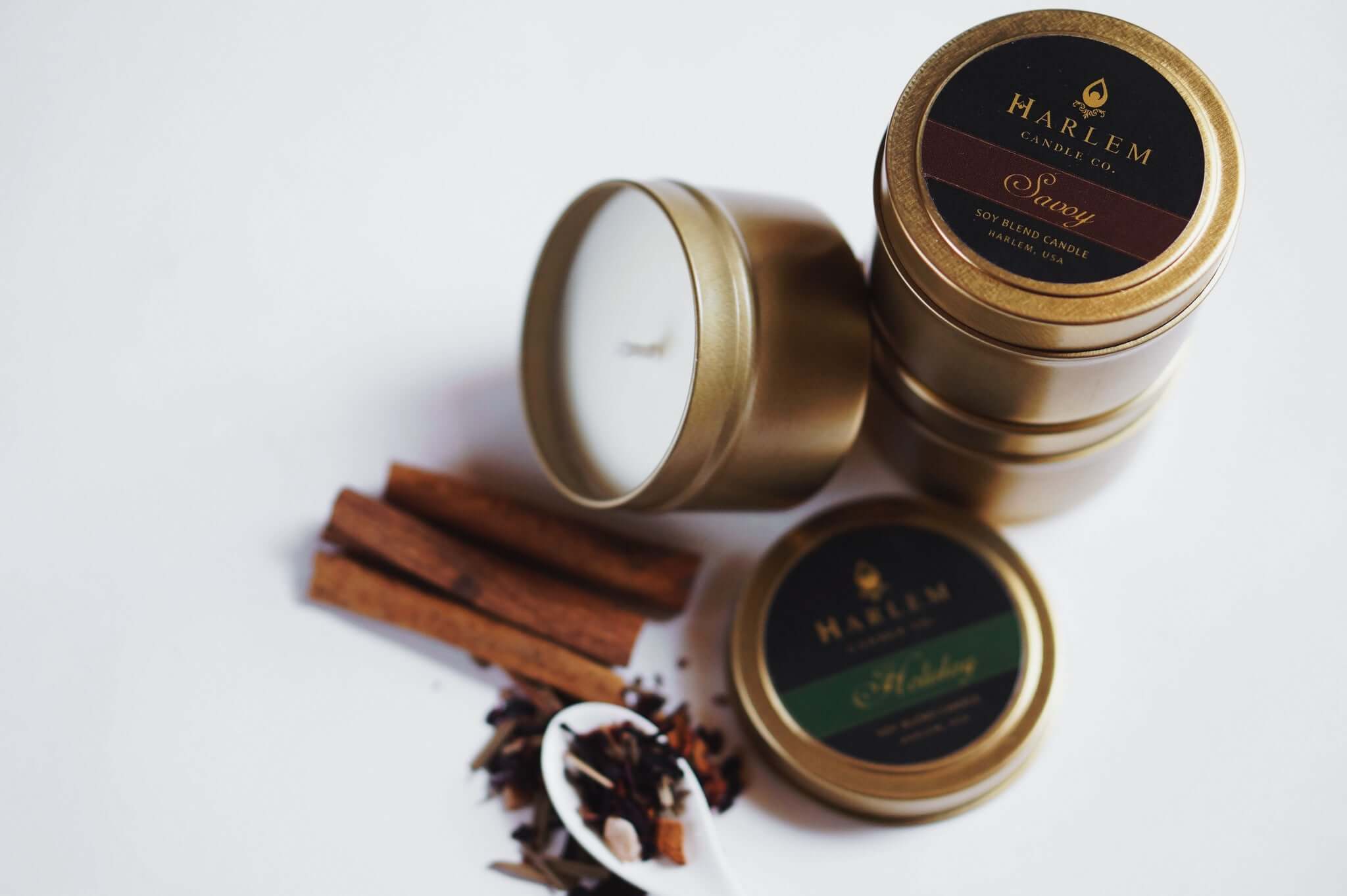 Our Savoy travel tin candle sitting on top of other travel tins displayed beautiful with cinnamon sticks on a white table.