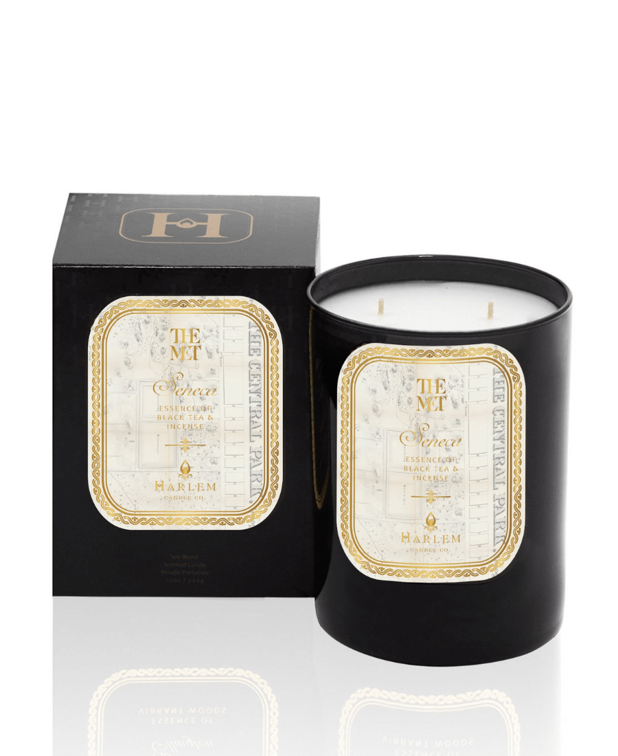 The black glass Met Seneca 12 oz two wick candle on a white background sitting next to its decorative box.