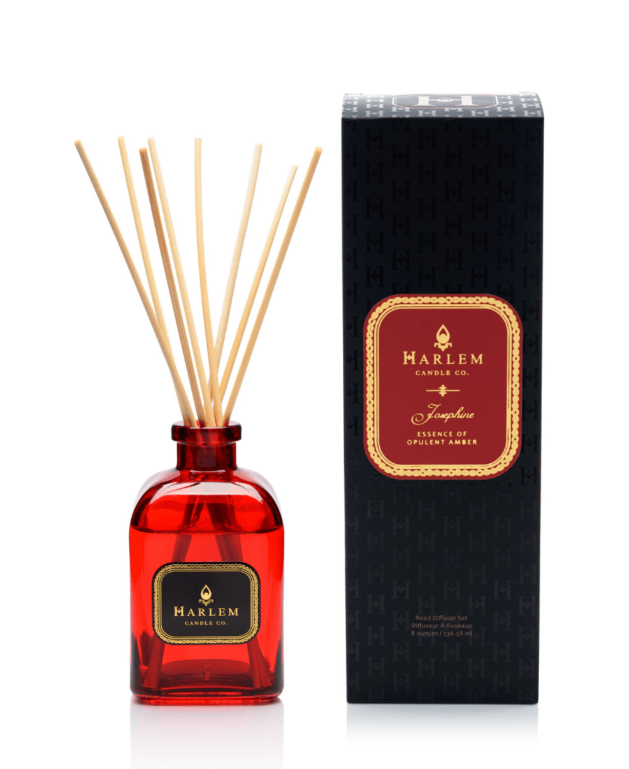 Our 8 fluid oz. Josephine Reed Diffuser with reeds, in a red glass vessel sitting next to its decorative box on a white background.