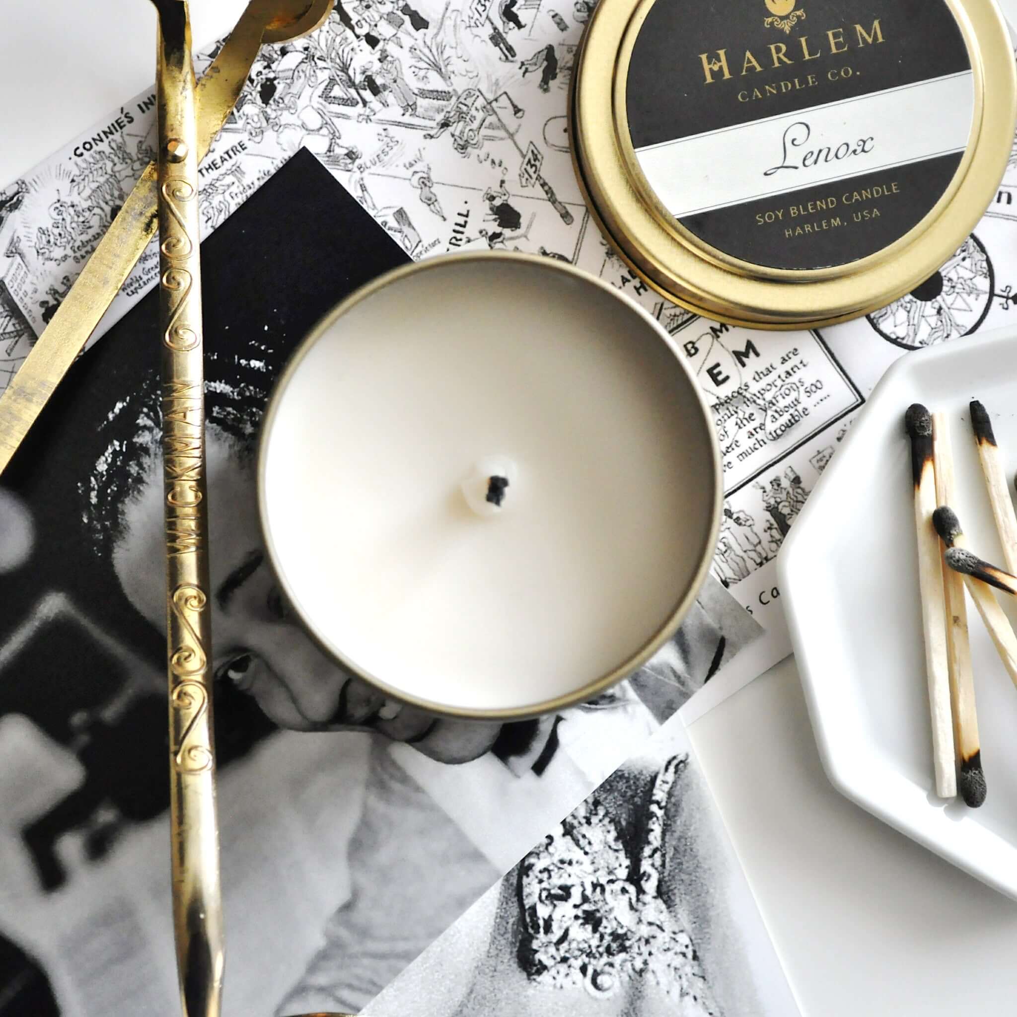 Our stunning Lenox travel candle in a  gold metal tin sitting atop our black and white harlem map..