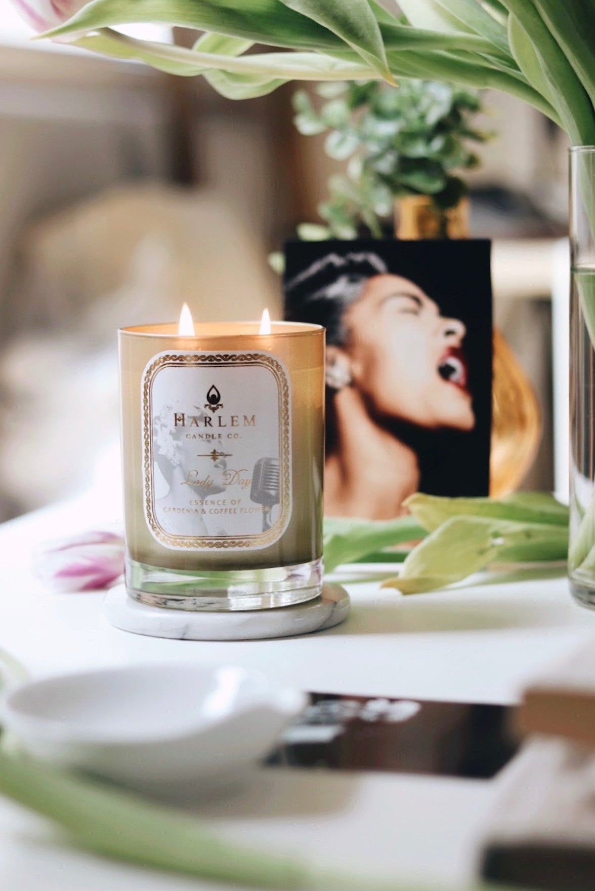 Lifestyle image of our Lady Day candle with green leaves in the background.