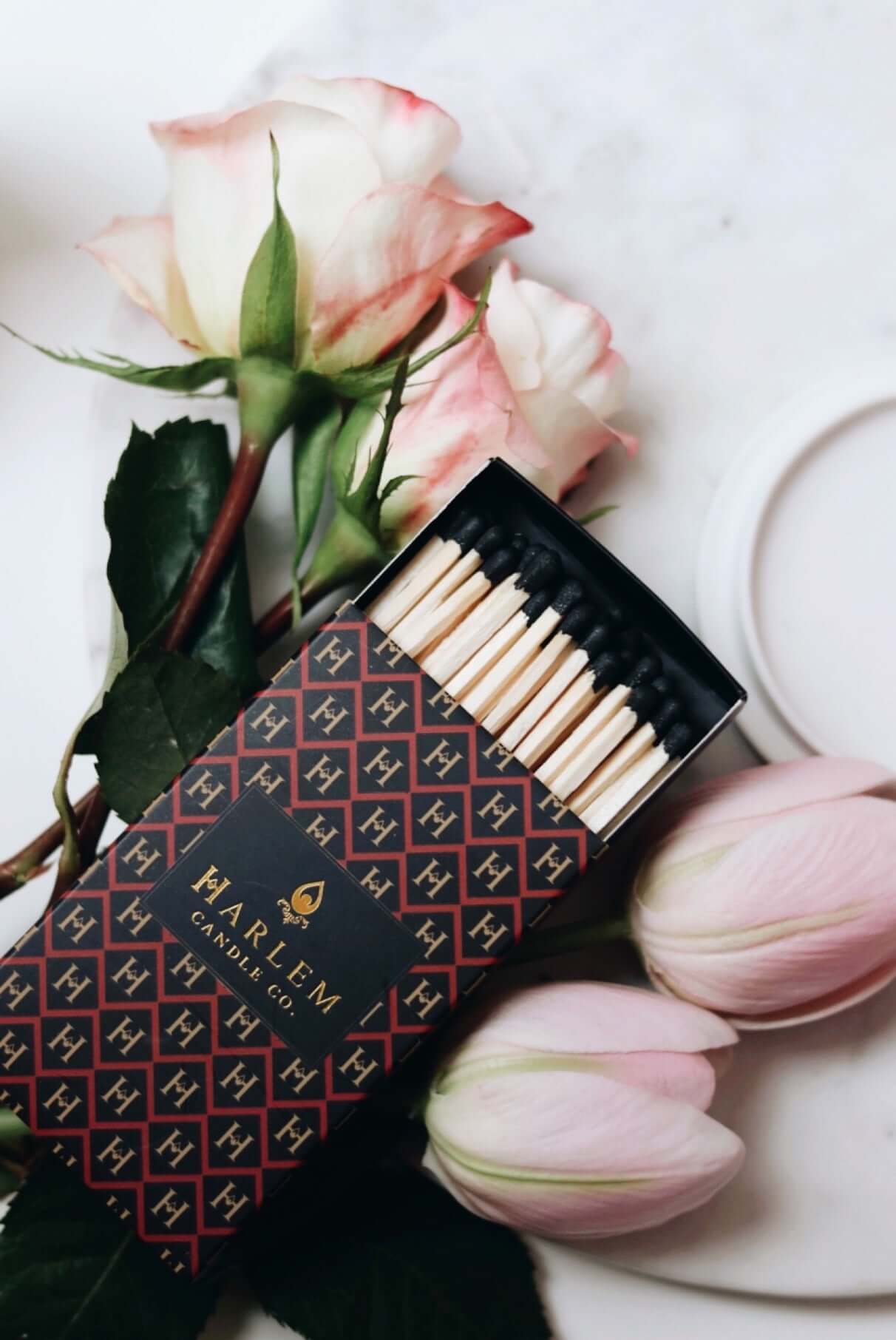 Red, black and gold Match box containing 3 inch matches with black tips.  The box has the Harlem H pattern in an art deco style printed on the box.  The image is on top of flowers.