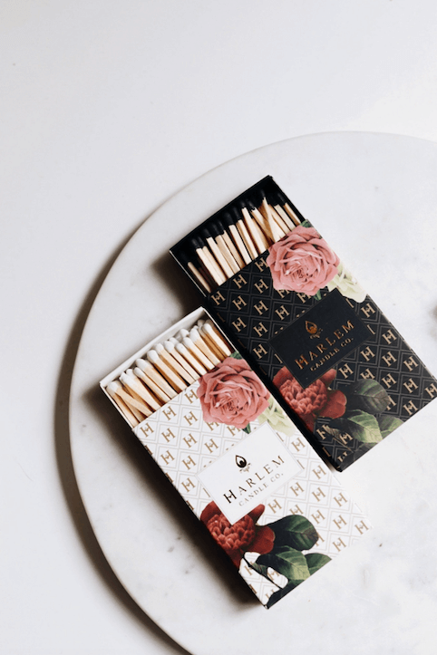 A lifestyle image of two of our match boxes, one white and one black, both floral art deco sitting on a white porcelain plate with a white background.