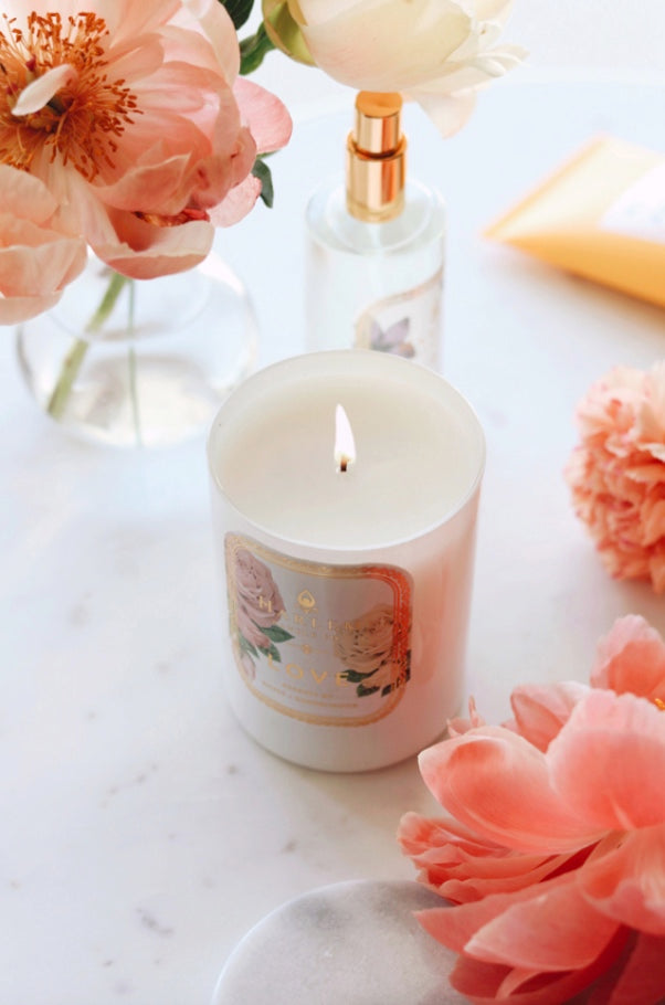 Lifestyle image of our love candle with peach flowers surrounding it.