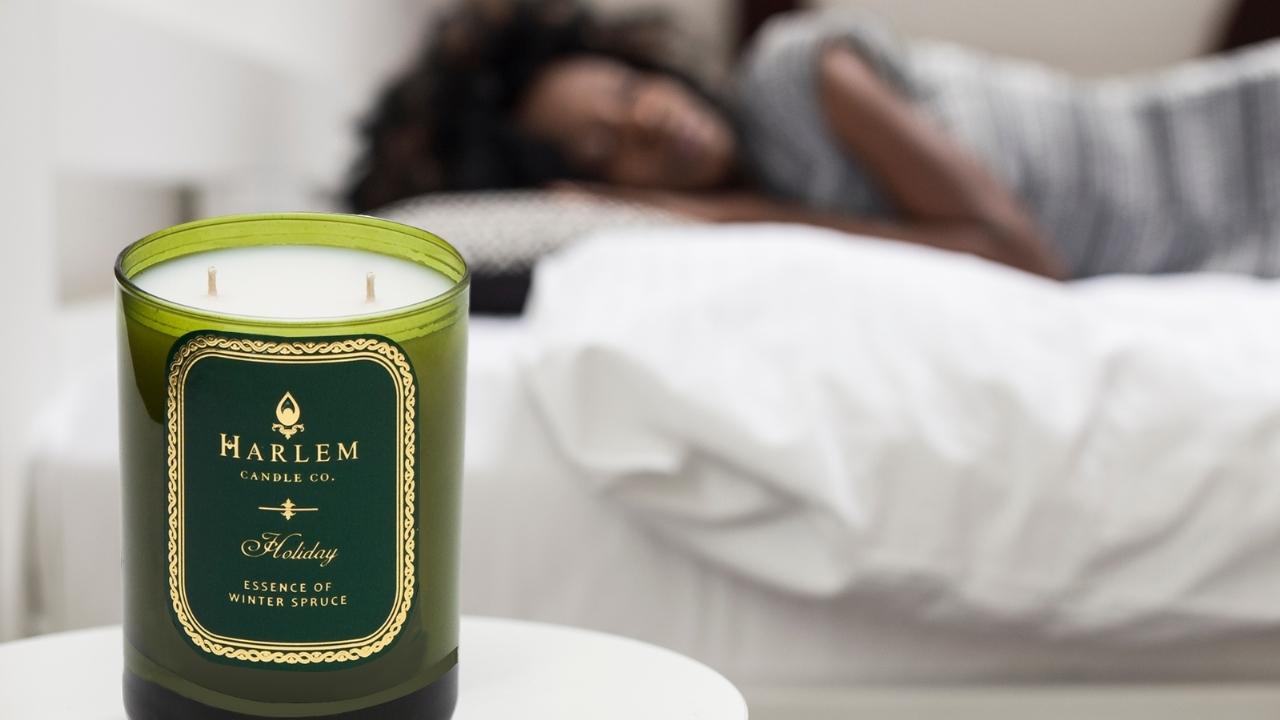 The Holiday luxury candle beside a bed.
