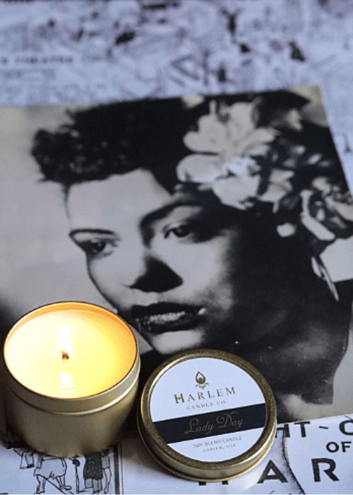 Gorgeous lifestyle image of the lit, 1 wick Lady Day 4 oz travel candle on top of a black and white harlem nights map and a black and white photograph of Billie Holiday.