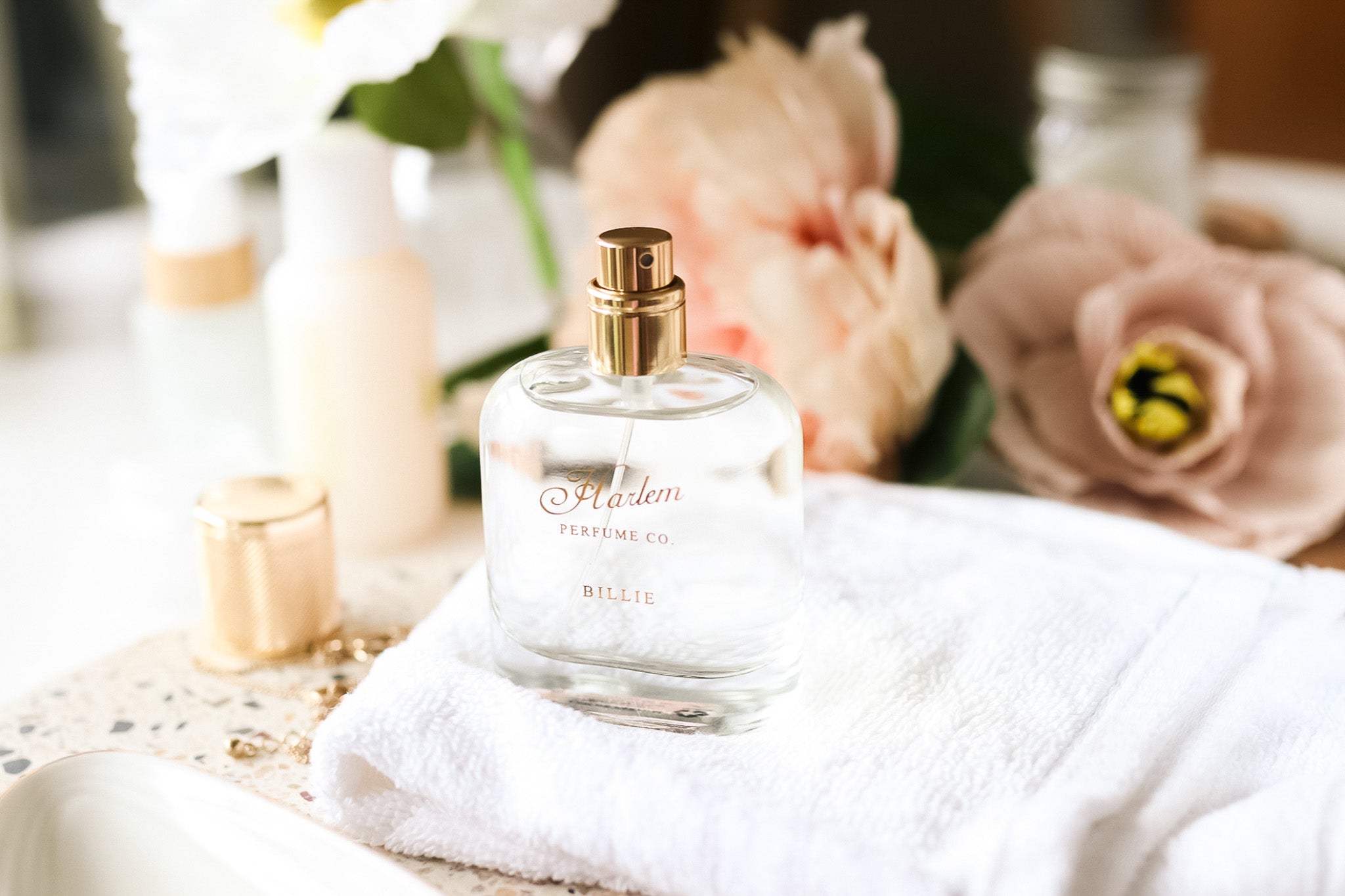 This is a lifestyle image of the "Billie" Eau de Parfum with the cap resting on a granite counter and flowers in the background. 