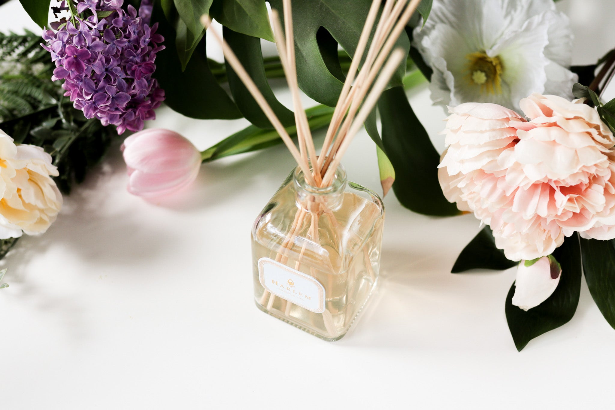 This is an image of a clear glass "Dream" Botanical Diffuser bottle with purple, white, and pink flowers in the background.