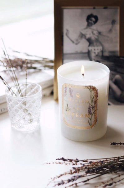 This is a lifestyle image of our dream candle in a lifestyle setting, with a beautiful image of a woman in a swimsuit in a frame behind it.