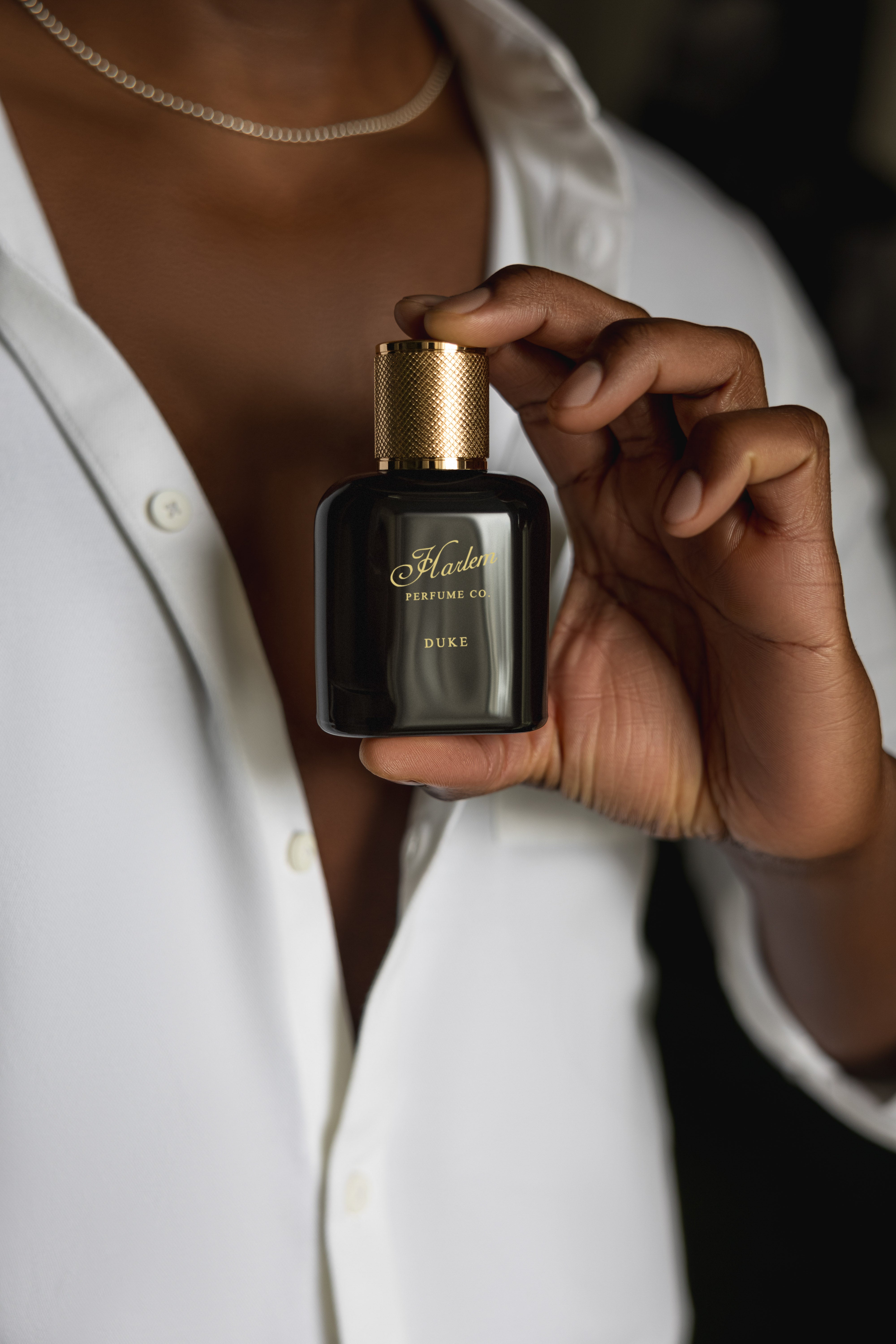 This is an image of our Duke perfume bottle, held by a man's hand against his chest as he wears a white button down shirt.
