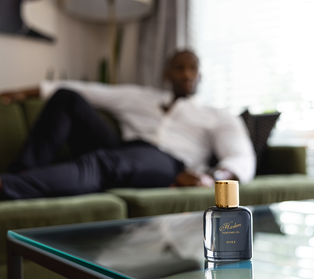 This is an image of our dark grey Duke perfume and with man sitting casually on a couch in the background.