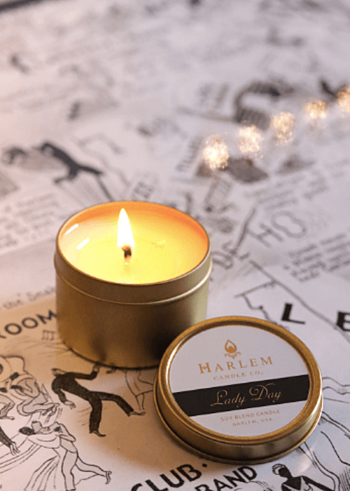 Gorgeous lifestyle image of the lit, 1 wick Lady Day 4 oz travel candle on top of a black and white harlem nightclub map.