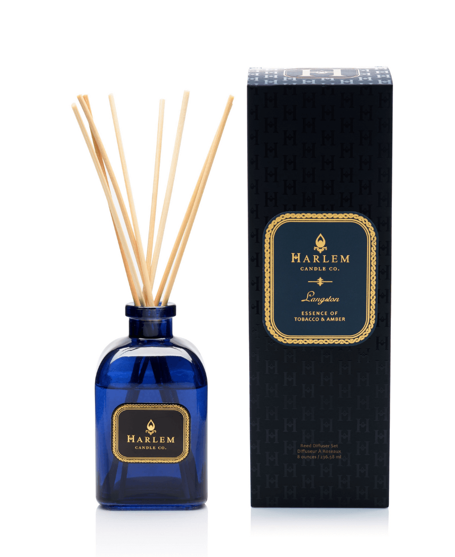 Our 4 fluid oz Langston Reed Diffuser with blue glass and reeds placed in diffuser glass sitting next to its decorative box with a white background.
