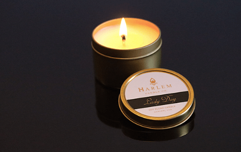 Gorgeous lifestyle image of our softly burning 1 wick Lady Day 4 oz travel candle on top of a black background.