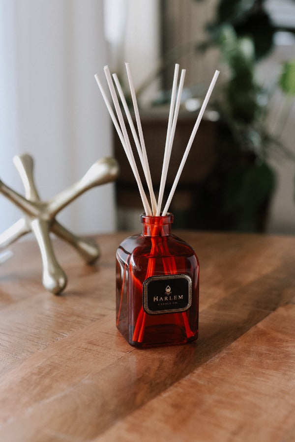 Our 8 fluid oz. Josephine Reed Diffuser with reeds, in a red glass vessel sitting on a wooden table.