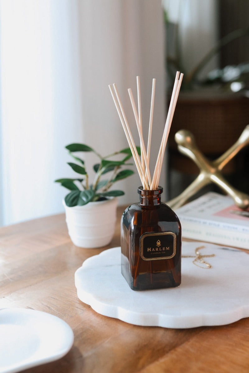 Our 8 fluid oz. Savoy Reed Diffuser with reeds, in a brown glass vessel sitting on a wooden table.