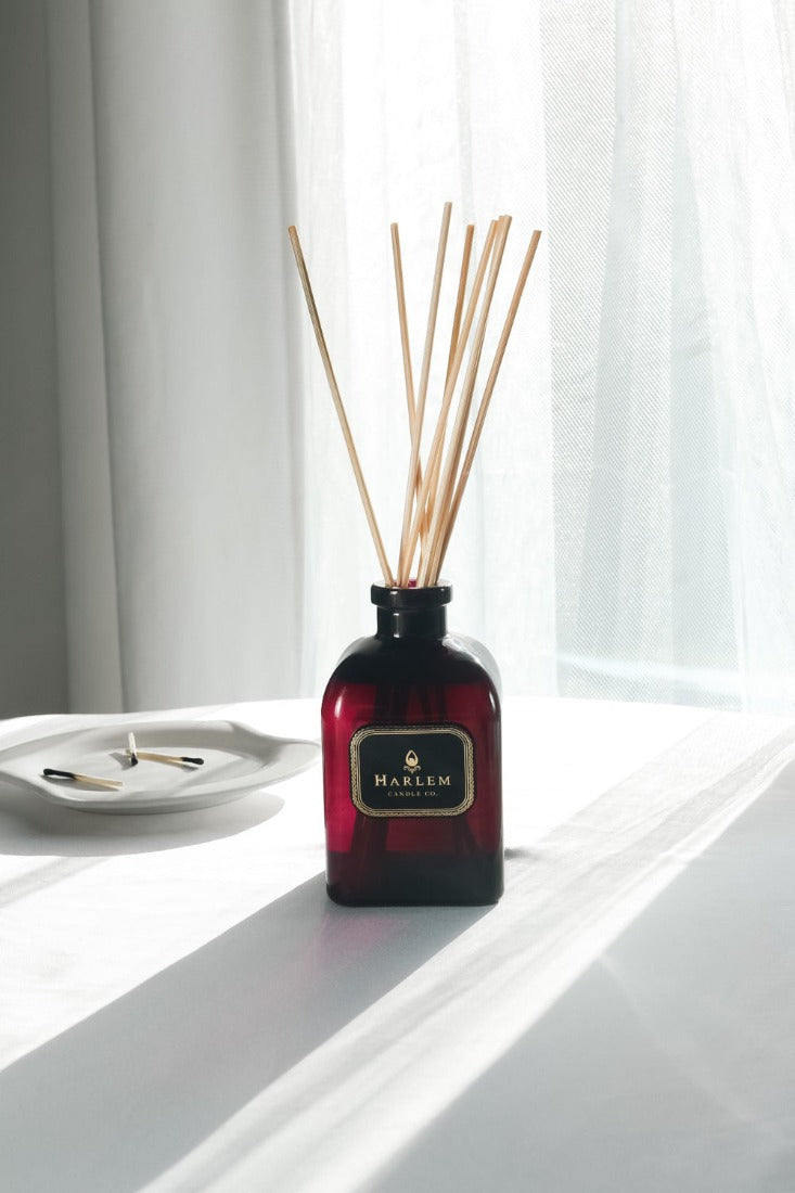 Our 8 fluid oz. Speakeasy Reed Diffuser with reeds, in a purple glass vessel sitting on a white table.