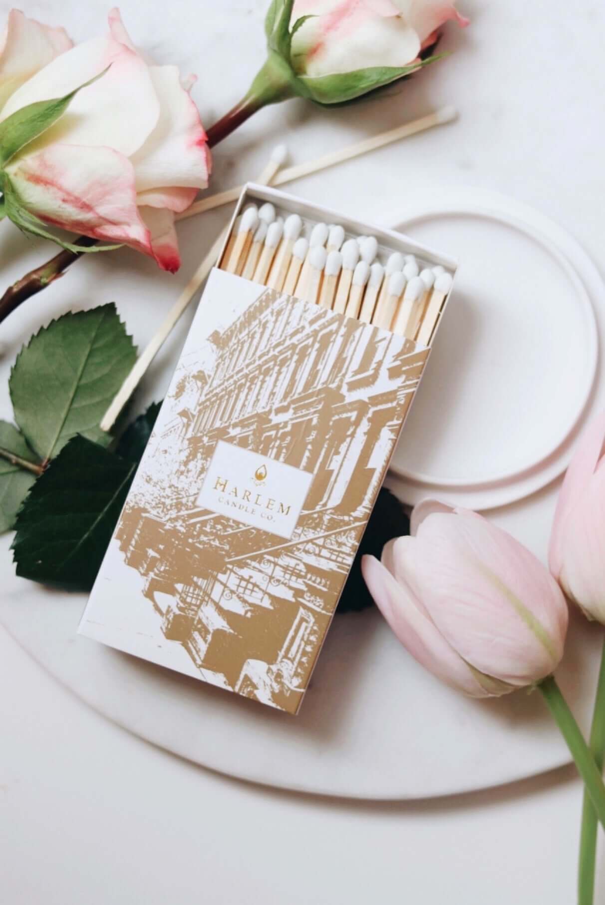 A lifestyle image of our Match Made in Harlem match box opened sitting atop a white plate with flowers surrounding with a romantic atmosphere.
