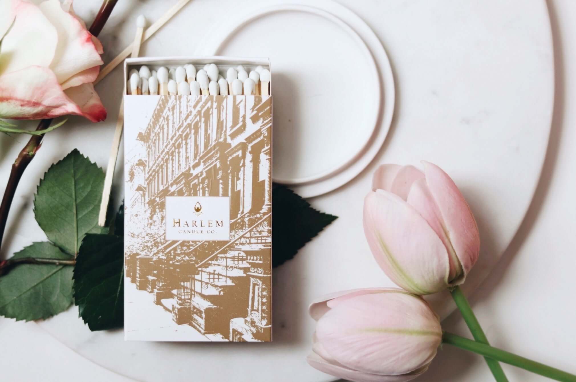 A lifestyle image of our Match Made in Harlem match box opened sitting atop a white plate with flowers surrounding.  