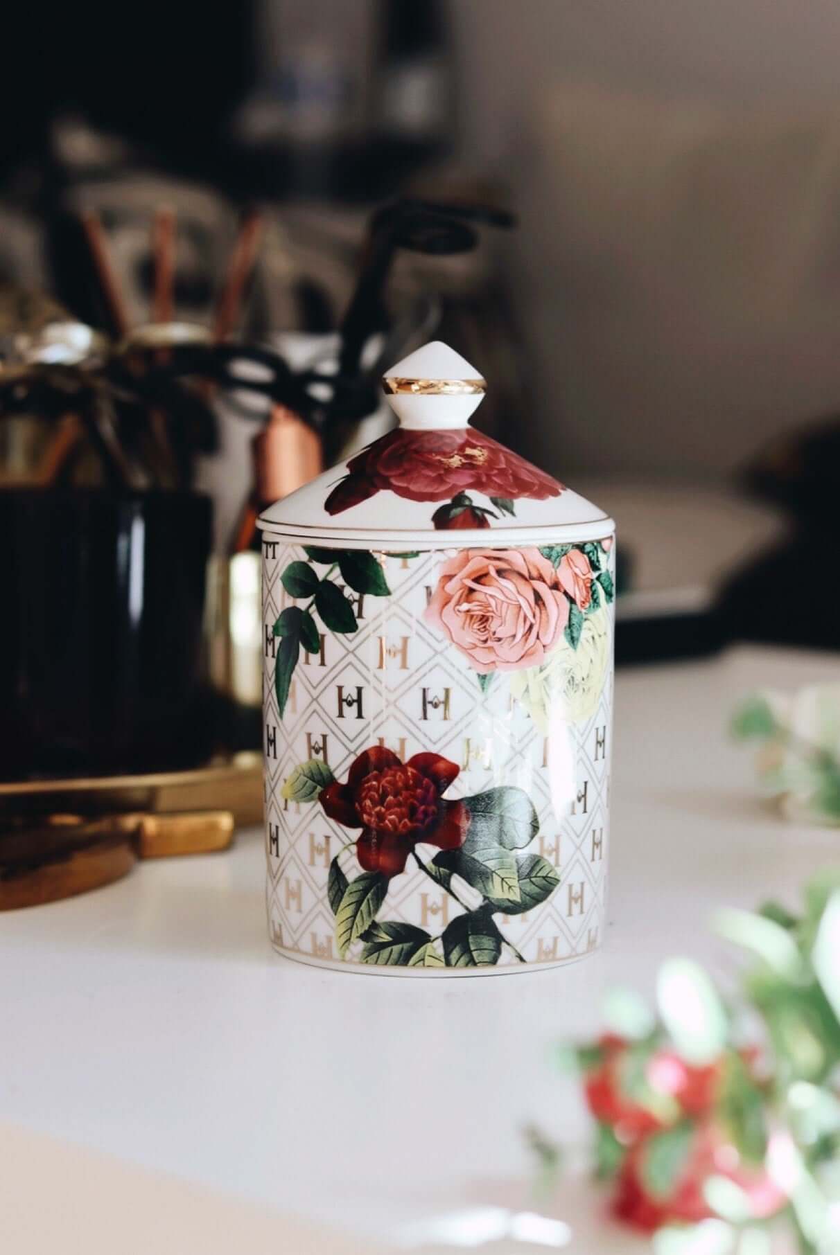 A stunning lifestyle image of Our “Lady Day” White Floral Ceramic Luxury Candle with lid  sitting on a white table with flowers.