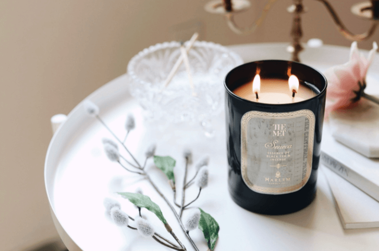 Gorgeous lifestyle image of the Met Seneca 12 oz candle sitting on a white side table with crystal and pussy willow on the table.