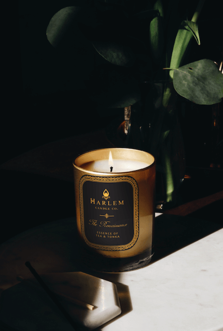 This is our Renaissance Candle,12 oz, 1 wick lit candle sitting on a marble table next to greenery. 