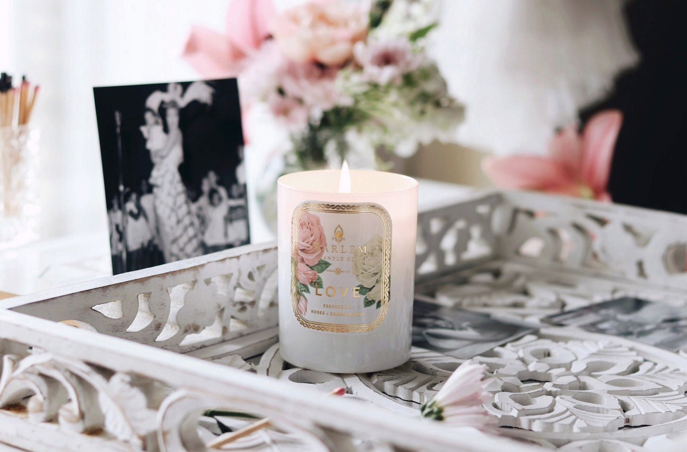 Lifestyle image of our Love candle with flowers and a black and white photo in the background