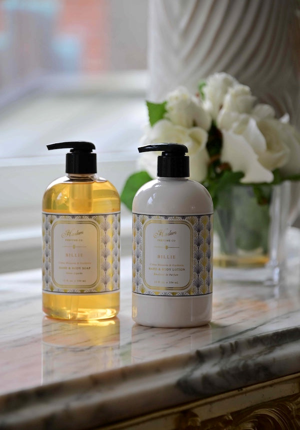 A lifestyle image of the Billie Soap and Lotion positioned next to each other with white flowers positioned in the background. 