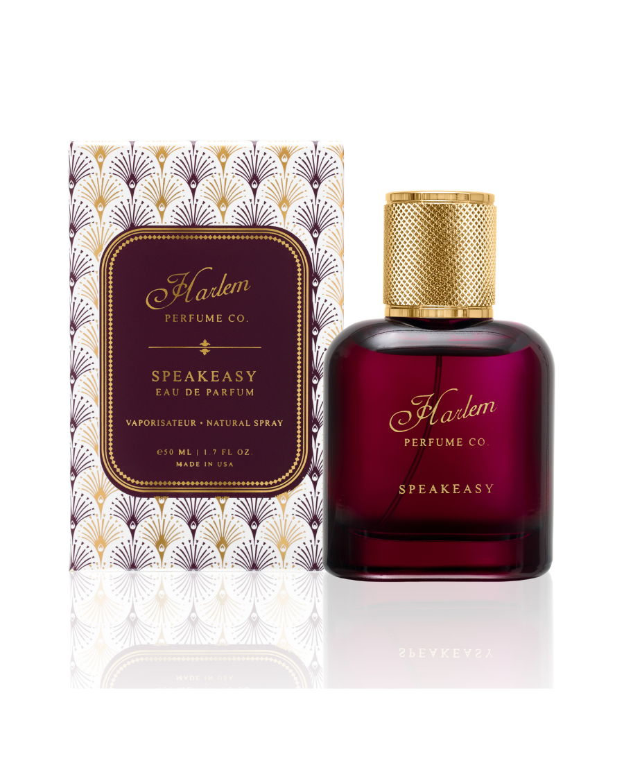 An image of our 50 ml / 1.7 oz Speakeasy eau de parfum in a rich burgundy bottle with a gold cap and the  Harlem Perfume Co logo on the bottle with the word Speakeasy in all caps in a block print font.  The bottle is pictured next to it's decorative box with a gold, burgundy and white art deco pattern.