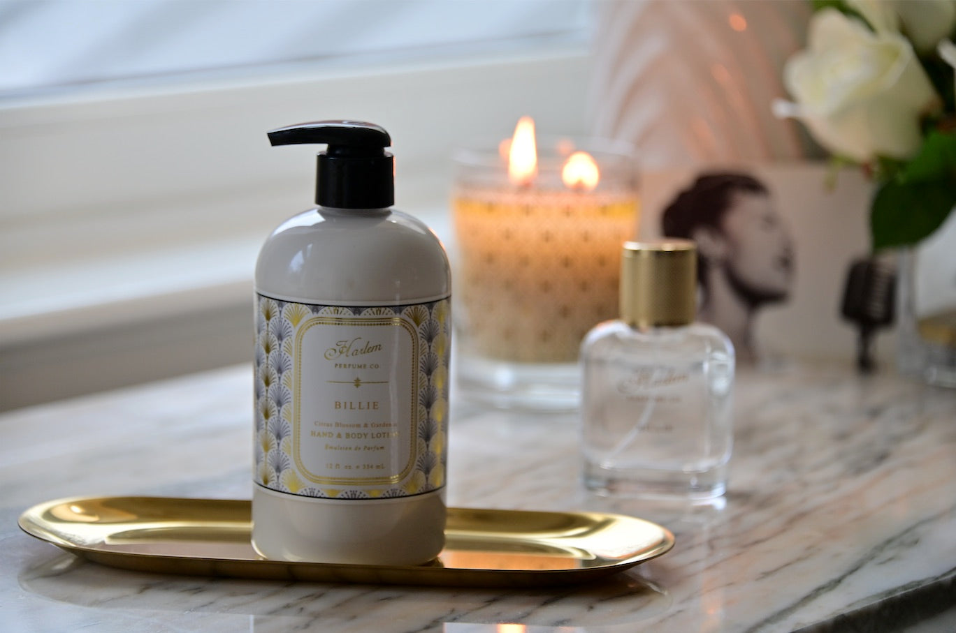 A lifestyle image of the Billie lotion with the Billie EDP and candle burning in the background.
